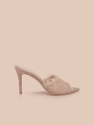 Introducing the Penn Mule: a beige mule with intricate lace detailing on the upper and a pointed toe, featuring a sleek stiletto heel and a memory foam insole for enhanced comfort, showcased against a light peach background.