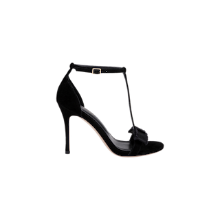 The Lerner Sandal is a black high-heeled T-strap sandal with a chic stiletto heel, ankle buckle, open toe, and decorative front bow. Showcasing a luxurious suede upper, this elegant shoe is displayed against a plain white background.
