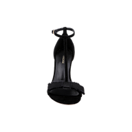 The Lerner Sandal is a black high-heeled T-strap sandal with an ankle strap and a bow detail on the front strap, featuring a suede upper and stiletto heel, shown from the front against a plain white background.