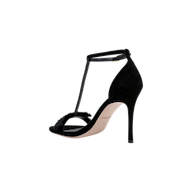 The Lerner Sandal is a black, suede T-strap sandal featuring a slim stiletto heel, open toe, and thin ankle strap, shown against a plain white background.