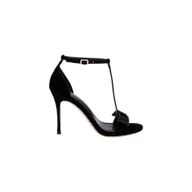 The Lerner Sandal is a black high-heeled T-strap sandal with a suede upper, ankle buckle, and open toe. Featuring a decorative bow detail on the front strap, it is presented against a plain white background.