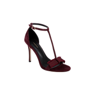Introducing the Lerner Sandal: a high-heeled T-strap sandal featuring a burgundy suede upper, an ankle buckle, and a decorative bow at the front. Complete with a sleek black insole and a thin stiletto heel for an elegant finish.