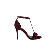 The Lerner Sandal features a burgundy suede upper with a T-strap design, stiletto heel, ankle buckle, open toe, and a decorative bow on the front, displayed against a plain white background.