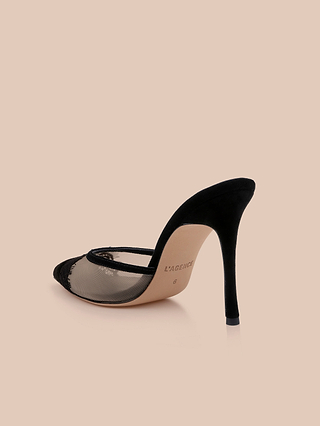 The Semois Mule features a black lace cap, pointed toe, mesh side panels, and a lavish black suede stiletto heel, shown against a simple beige backdrop. The sole is stamped with the L’AGENCE brand name.