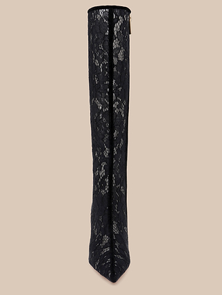 The Chambers Boot, a tall black lace-up design featuring a pointed toe and a sleek stiletto heel, is displayed from the front against a neutral beige background.