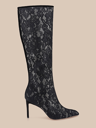 Introducing the Chambers Boot: a black knee-high boot with a pointed toe and stiletto heel, featuring a sheer floral lace overlay against a beige background—these stunning black lace boots are the epitome of elegance in high-heeled footwear.