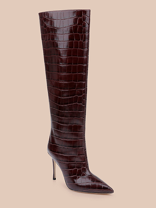 The Lafayette Boot is a tall, dark brown boot made from crocodile-embossed leather, featuring a pointed toe and high stiletto heel, beautifully presented on a beige background.