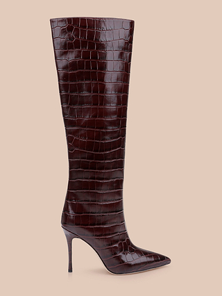 The Lafayette Boot is a tall silhouette in dark brown crocodile-embossed leather, featuring a pointed toe and a high stiletto heel, showcased against a beige background.