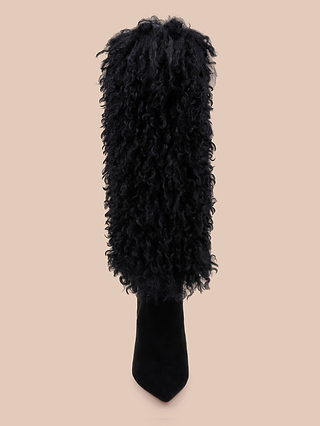 The Sheridan Boot—a single high-heeled, black boot featuring a tall shaft enveloped in curly, textured faux fur—stands out against a plain beige background.