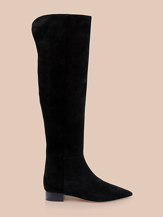 The Grand Boot is a black suede over-the-knee boot featuring a slightly pointed toe and low block heel, presented on a beige background in a side profile view with no visible embellishments.