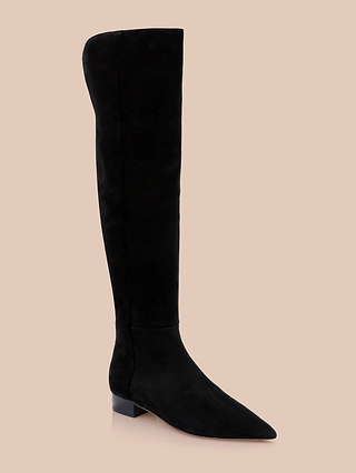 The Grand Boot is a black suede over-the-knee boot featuring a pointed toe and low block heel, shown against a plain beige background.