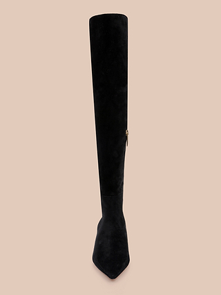 The Grand Boot is a single black suede over-the-knee boot featuring a pointed toe and side zipper, displayed upright against a beige background.