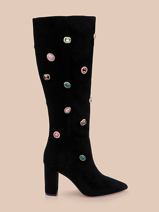 The Concourse Boot is a black suede knee-high boot with a block heel, adorned with colorful, round and oval jewel-like embellishments along the shaft; these embellished suede boots are photographed against a plain beige background.