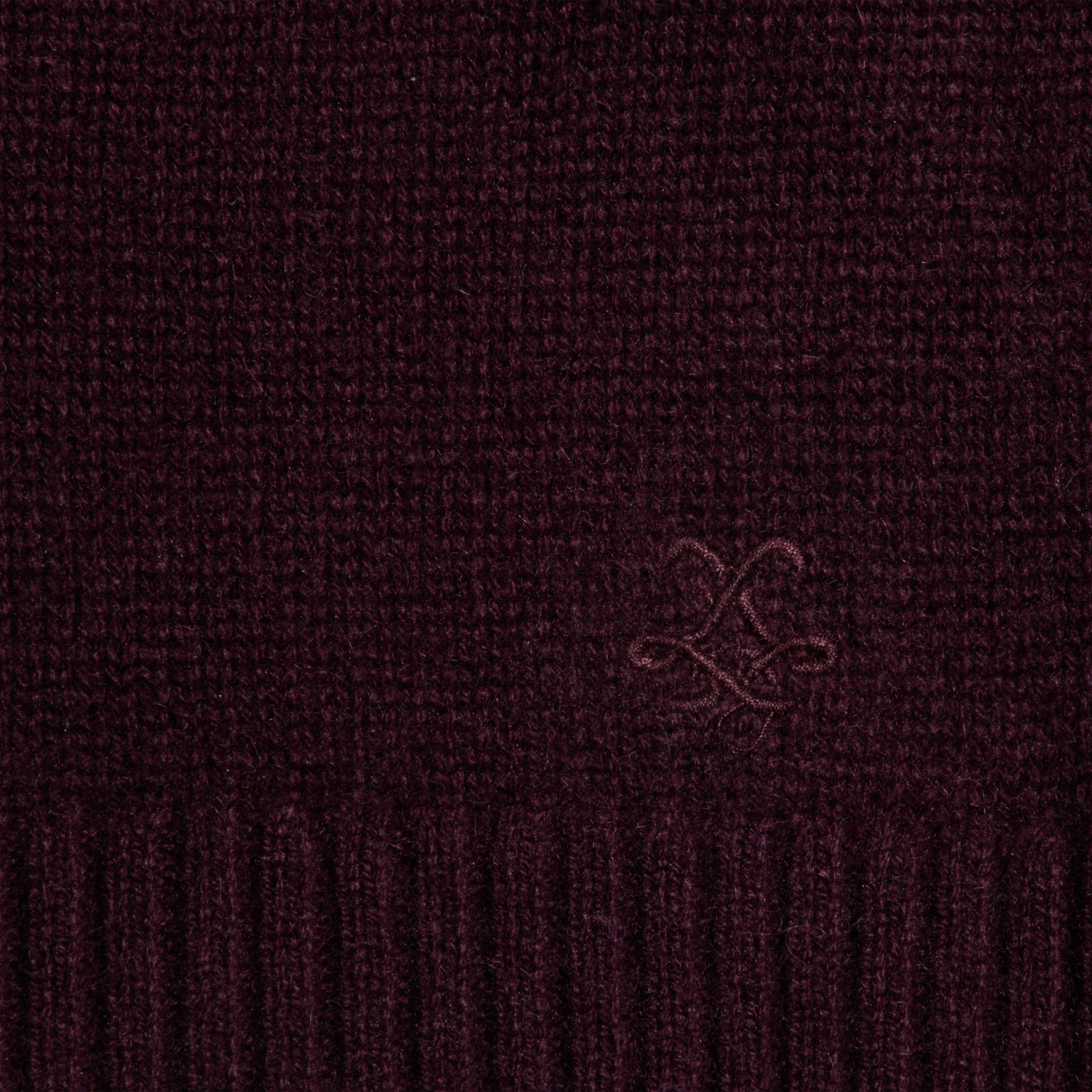 Close-up of a dark burgundy knitted fabric with a small, subtle embroidered logo and a ribbed edge at the bottom.