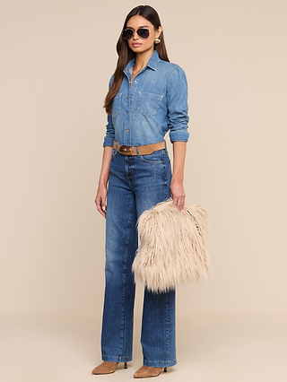 Woman in a denim shirt and jeans, wearing sunglasses, holding the Adelina Faux Fur Clutch as a statement accessory, accessorized with a tan belt and shoes, standing against a plain light background.