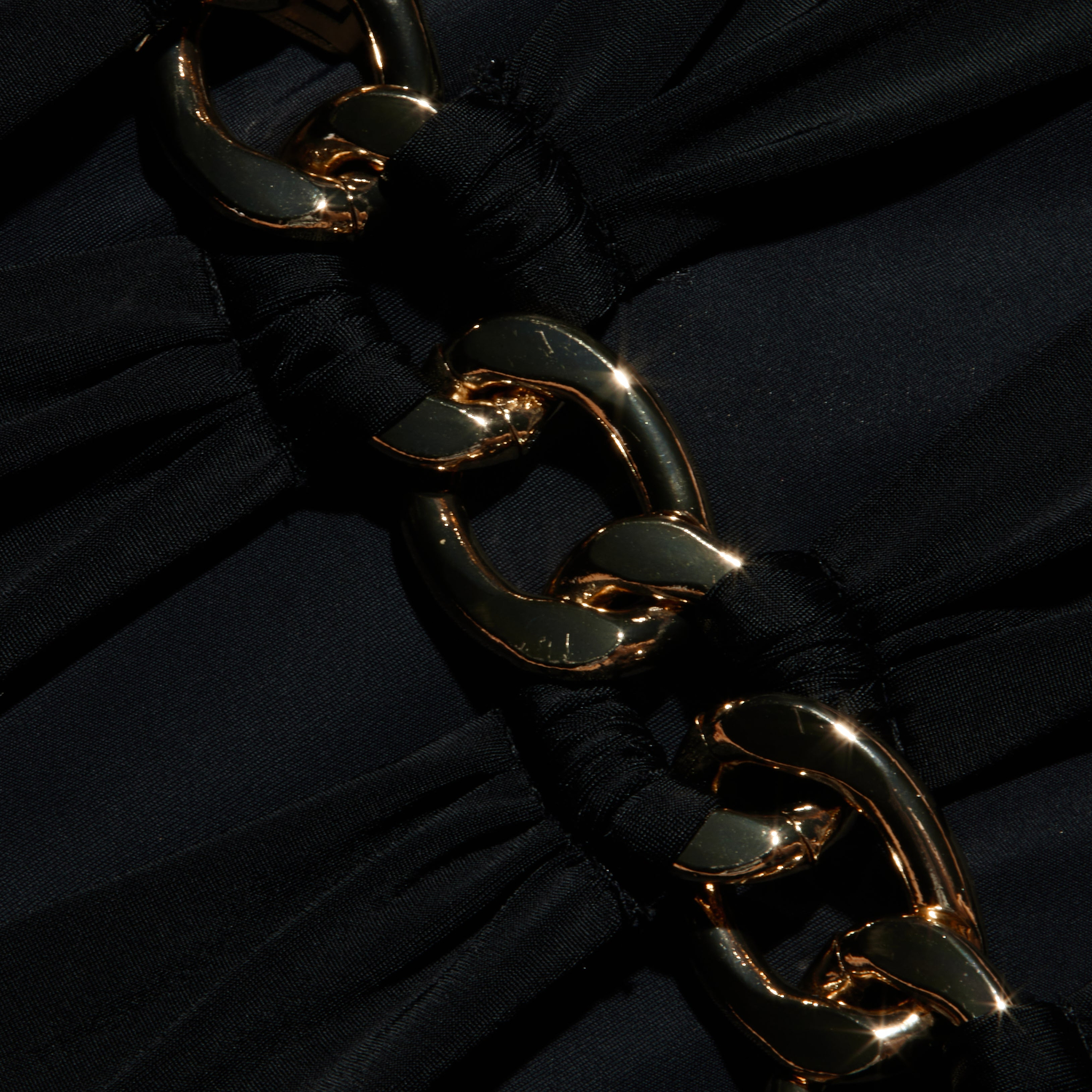 Close-up of shiny gold chain links intertwined with gathered black fabric on the Opus Halter One-Piece Swimsuit, creating an elegant and textured contrast between the metal and cloth—an accent reminiscent of high-end resort swimwear.