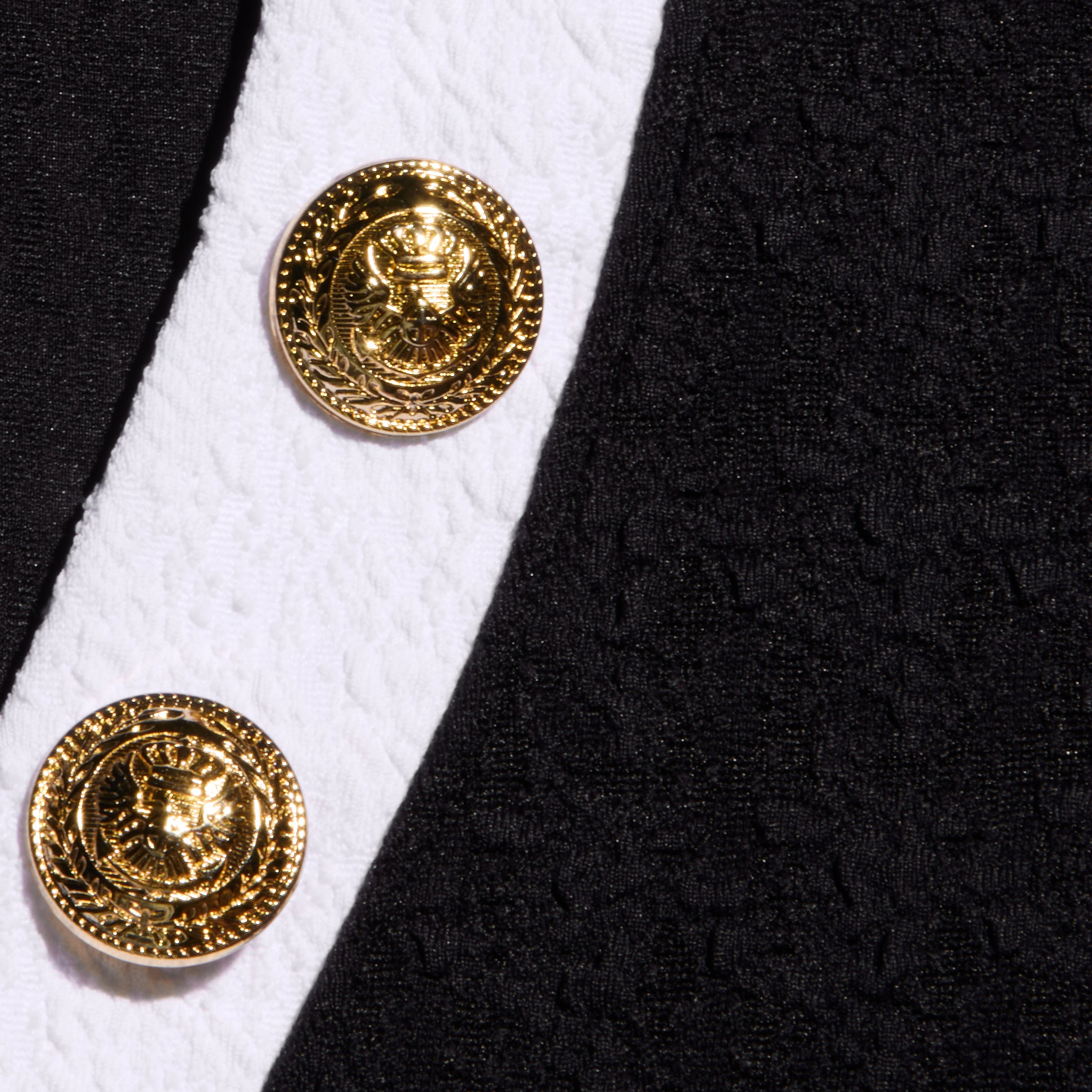 Close-up of the Laguna Rash Guard in black and white, featuring water-safe bouclé fabric and two gold eagle-embossed buttons for a stylish, polo-inspired look.