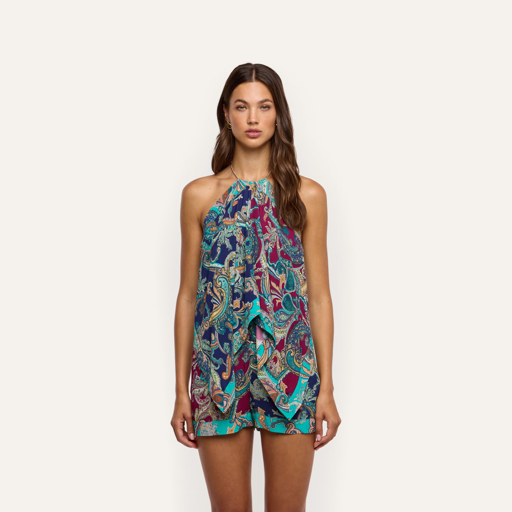 A woman wears a Kochi Cover-Up Top, a sleeveless, halter-neck resort wear piece featuring a colorful blue, teal, and magenta paisley print with a layered, draped front and chain details.