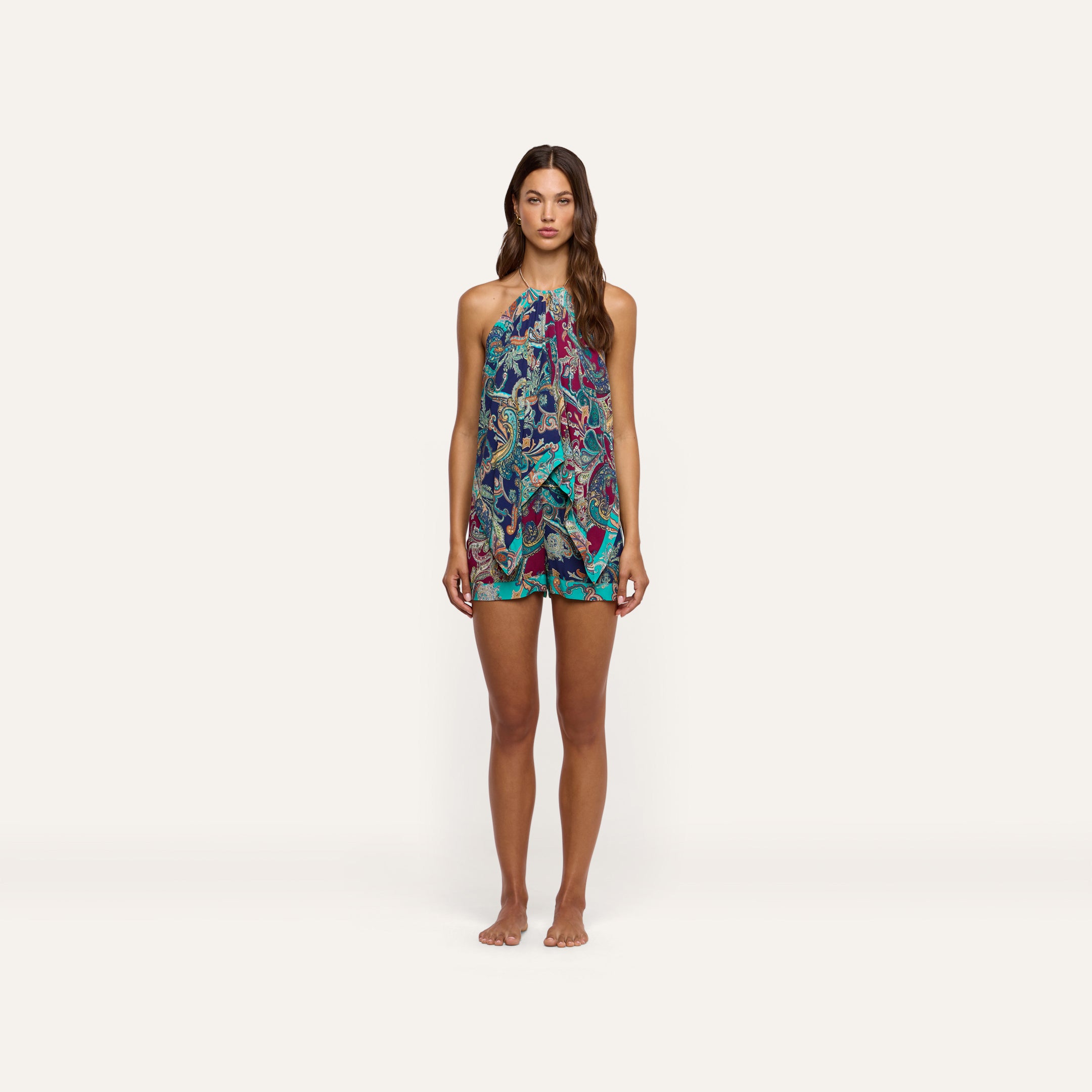 A model wears a vibrant blue and magenta paisley print Kochi Cover-Up Top with gold chain details and matching shorts.