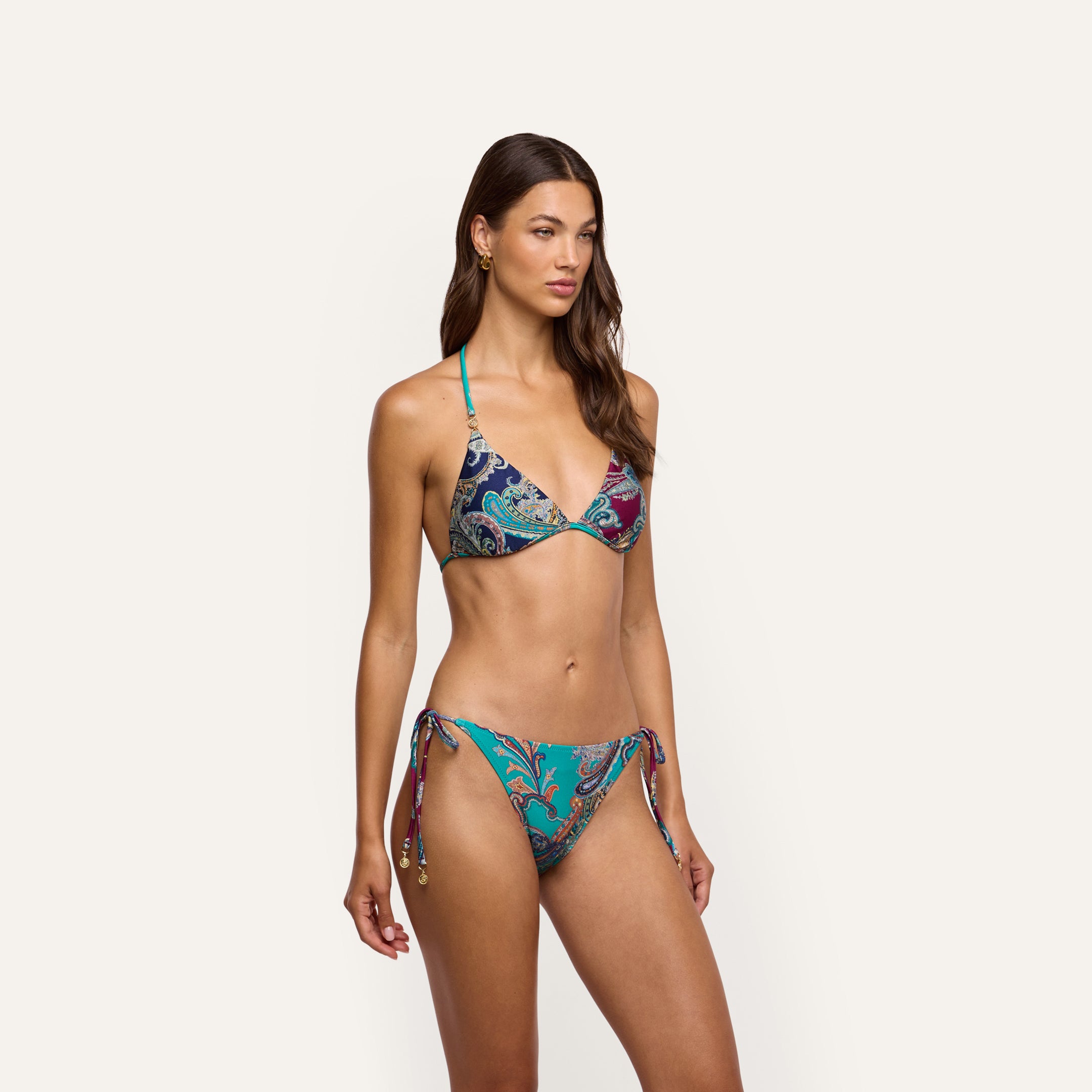 A woman wearing an Annabelle Bikini Top in a paisley-print triangle silhouette with teal straps and side ties.