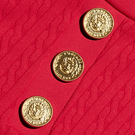 Three ornate gold buttons with embossed designs are sewn onto the textured red fabric with a wavy pattern of the Coco Mini Skirt Cover-Up, making it an elegant detail for your swim skirt or cover-up ensemble.