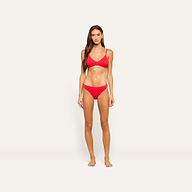 A woman with long brown hair stands against a plain light background, wearing the bright red Playa Bikini Top and no shoes, looking directly at the camera with a neutral expression.