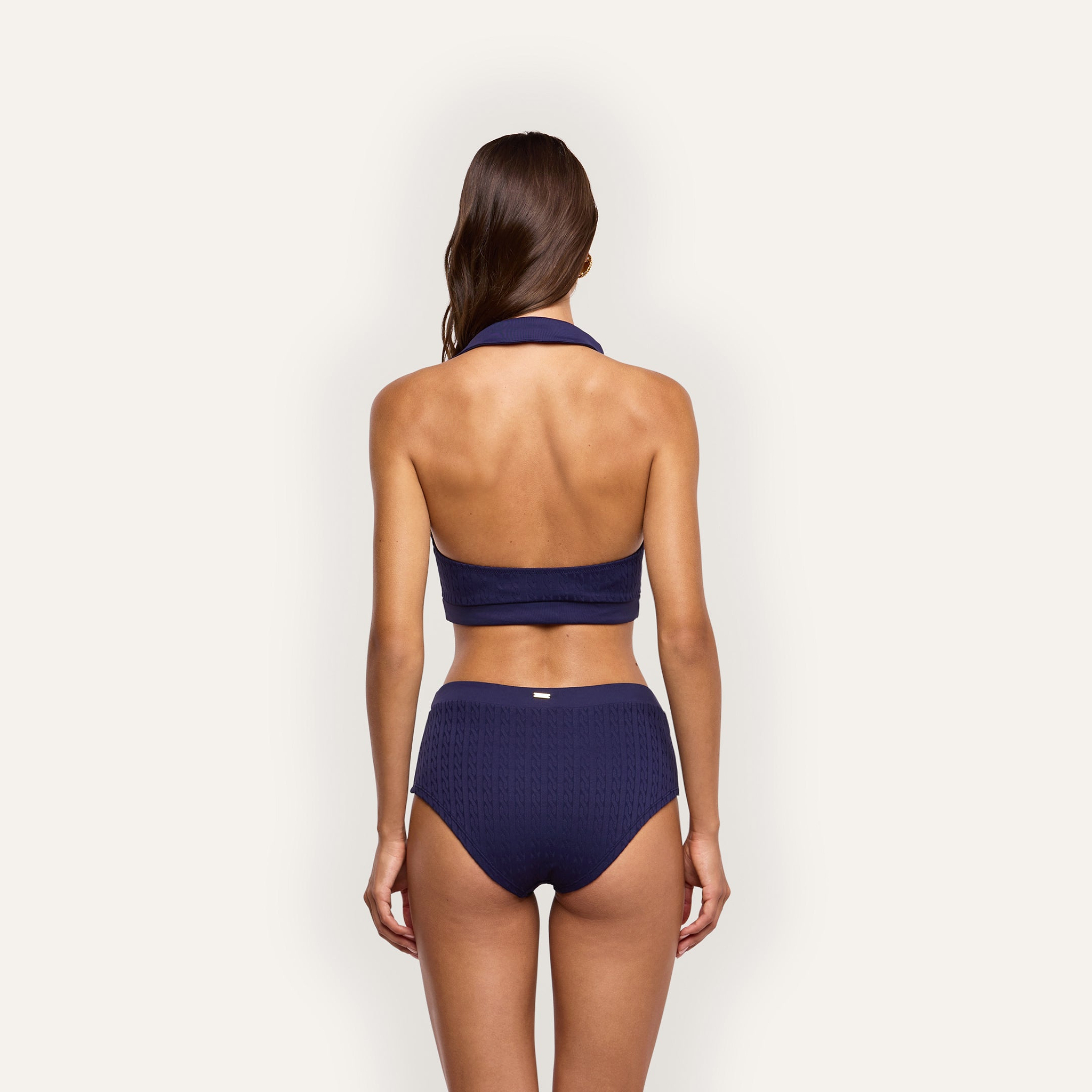 Back view of a person wearing a dark blue Coronado Bikini Bottom in textured, cable-knit UPF 50 fabric with cheeky swim shorts.