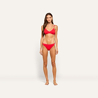 A woman stands facing forward, wearing the Jean Bikini Bottom in red, featuring a high-leg cut and textured swim fabric, against a plain, light-colored background.