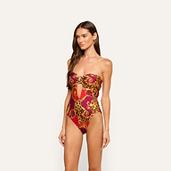 A woman stands against a plain light background wearing the Emilia Bandeau One-Piece Swimsuit, featuring gold and red baroque and leopard print accents.