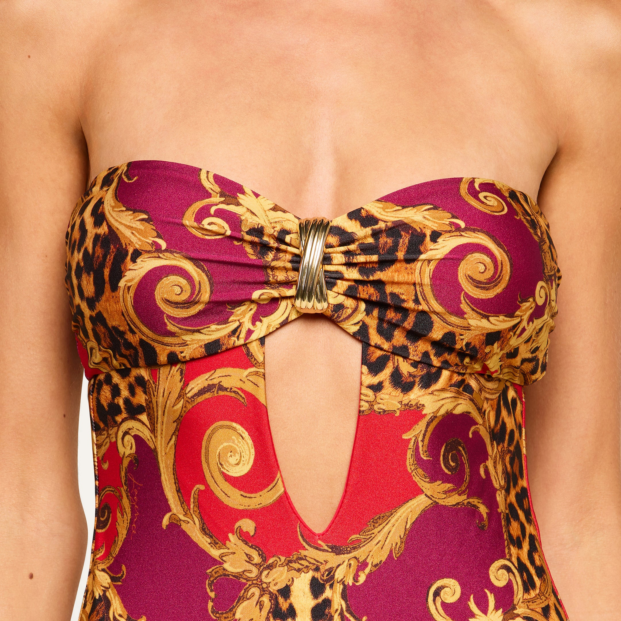 Close-up of the Emilia Bandeau One-Piece Swimsuit, showcasing a gold and red baroque and leopard print pattern with a bandeau design featuring a front cutout held by a decorative metallic clasp at the center.