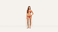 A woman stands barefoot against a plain white background, wearing a striking red and gold bikini. She has long brown hair and looks forward confidently, with one hand on her hip.