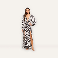 A woman stands barefoot against a plain light background, wearing the Sara Maxi Cover-Up Dress—a long zebra print dress with long sleeves, a deep V-neckline, and a high side slit.