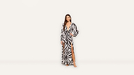 Woman standing in a long, zebra-print dress with a deep V neckline and a high slit, posing barefoot against a plain white background. The bold animal print adds a striking touch to her elegant look.