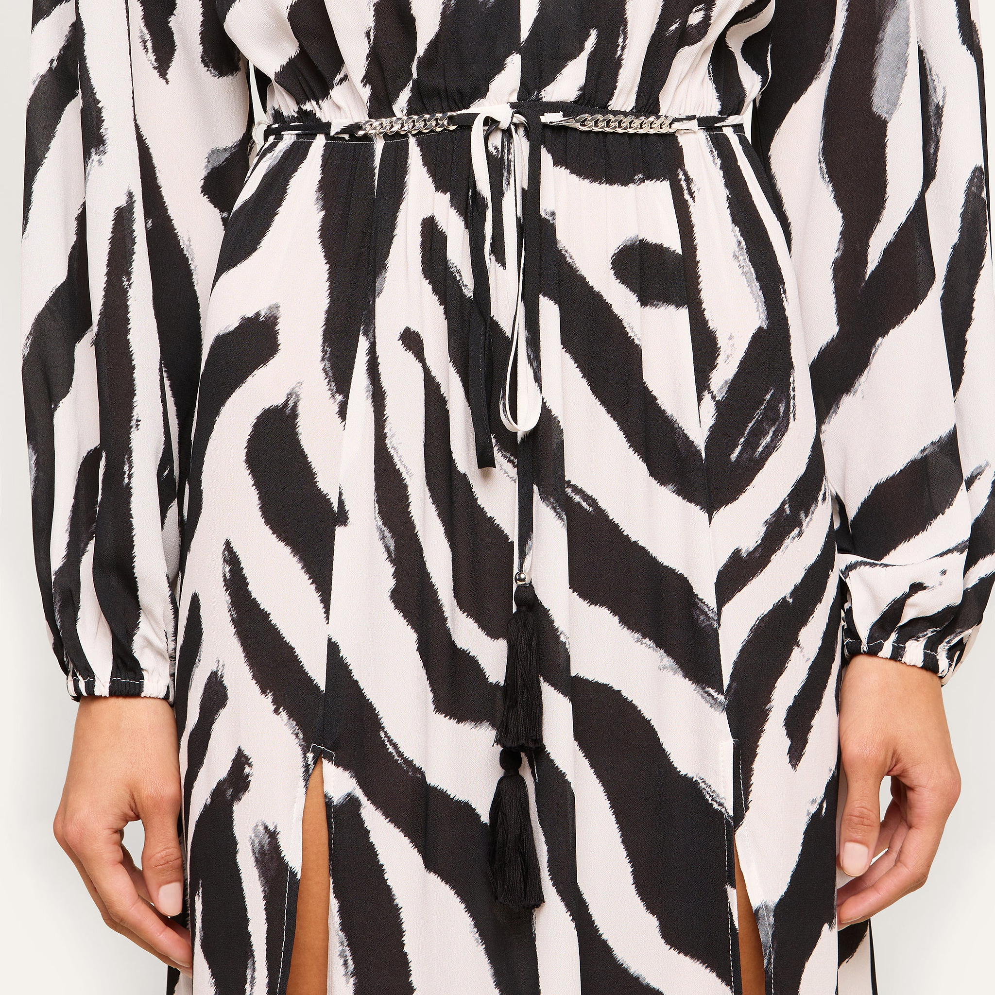 Close-up of a person wearing the Sara Maxi Cover-Up Dress, featuring a black and white zebra print with a thin waist belt and tasseled cords, highlighting the dress’s unique pattern and details.