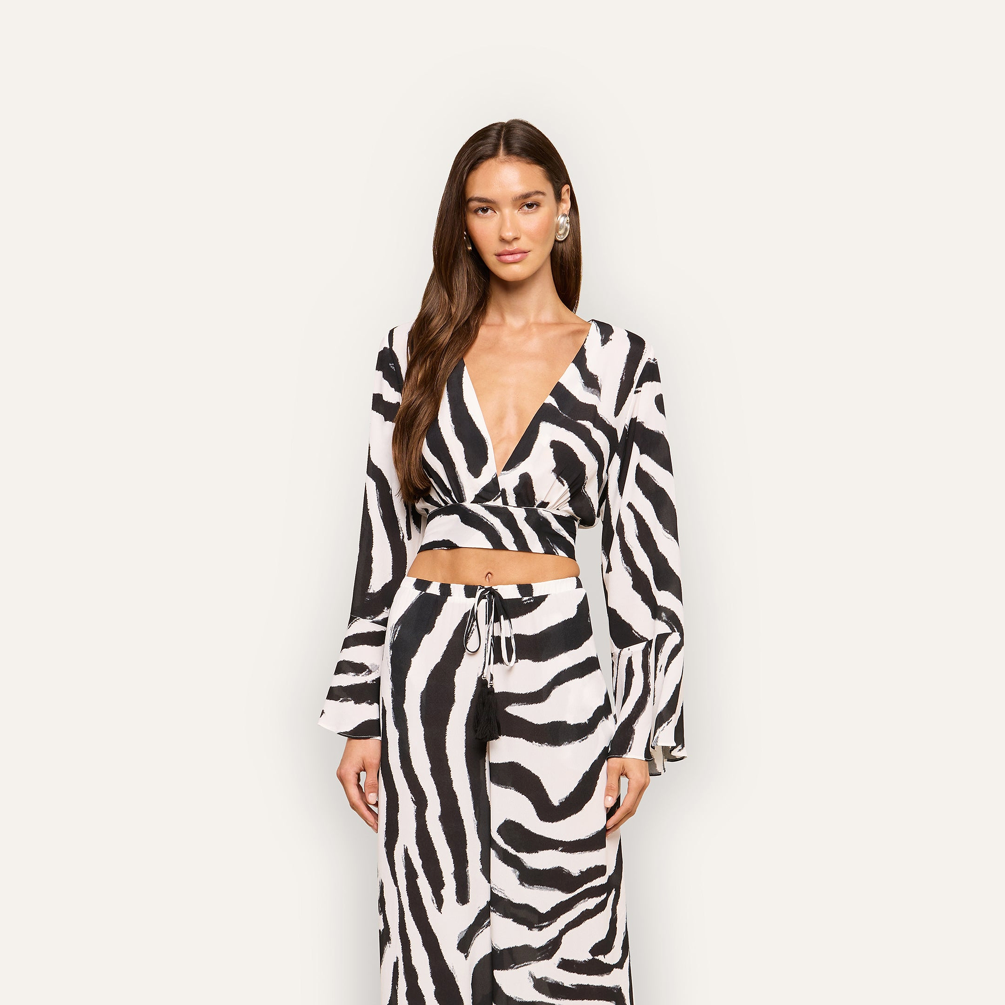 A woman with long brown hair wears the Ambala Cover-Up Top with a zebra-print wrap design and a matching skirt, standing against a plain light background.