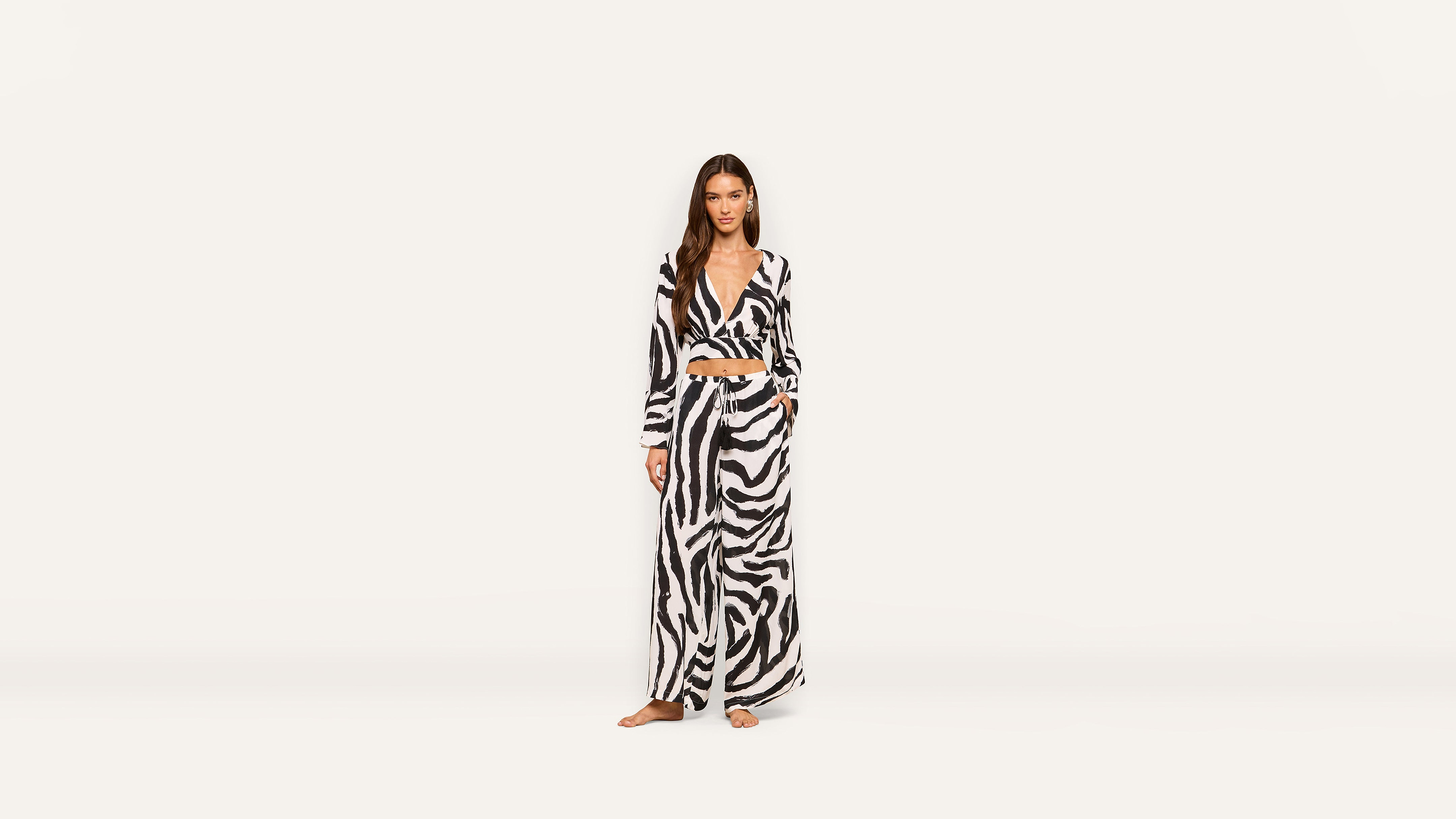 A woman stands barefoot in a long-sleeved, black and white zebra-print wrap top and wide-leg pants against a plain white background.