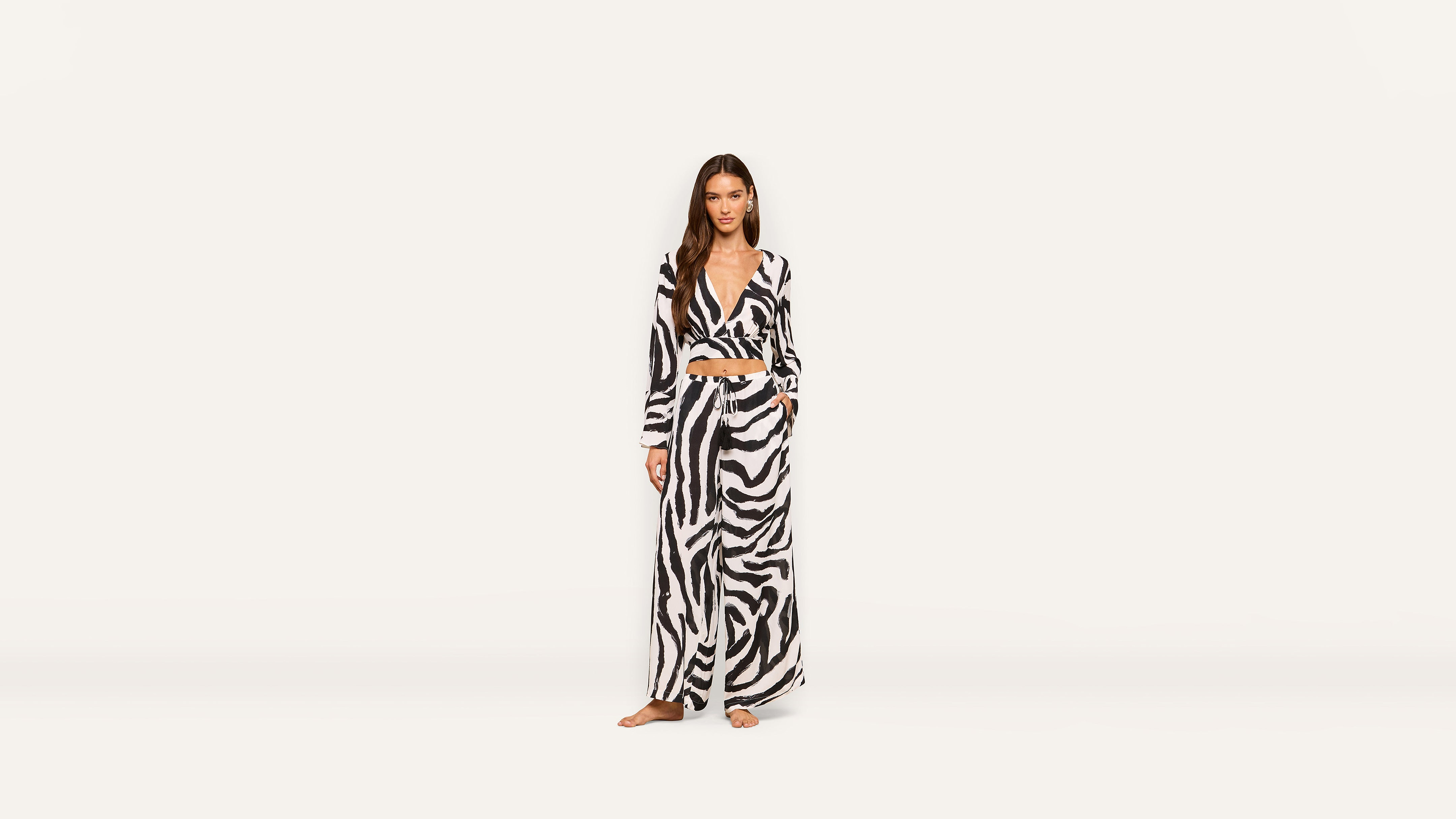 A woman stands barefoot in a long-sleeved, black and white zebra-print wrap top and wide-leg pants against a plain white background.