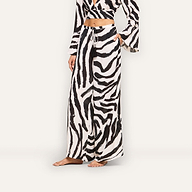 A person stands barefoot against a plain background wearing the Geraldine Cover-Up Pant in a zebra print, paired with a matching long-sleeve crop top. The person’s face is not visible.