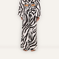 A person stands barefoot, seen from behind, wearing the Geraldine Cover-Up Pant—wide-leg zebra print pants—paired with a matching long-sleeve top that ties at the back.