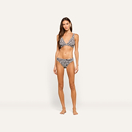 A woman with long brown hair stands barefoot against a plain light background, wearing a zebra print bikini and the Nicole Bikini Bottom, her arms relaxed at her sides and her expression neutral.
