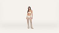 A woman stands on a white background wearing a cream-colored bra, matching underwear, and sheer, glittery pants.