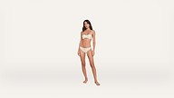 A woman stands barefoot against a plain white background, wearing a light-colored strapless bra and matching underwear.