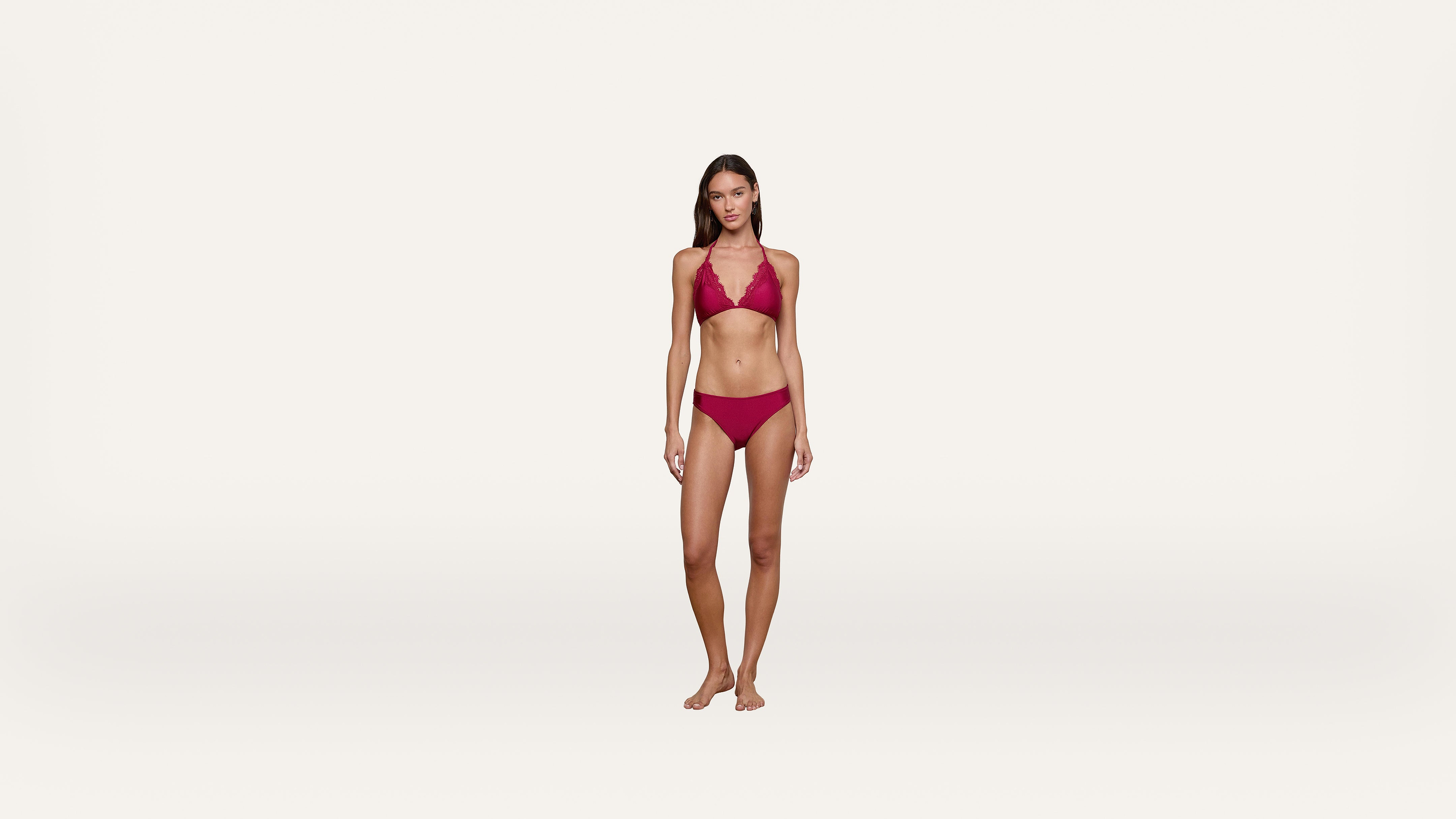 A woman stands barefoot on a plain white background, wearing a red bikini.