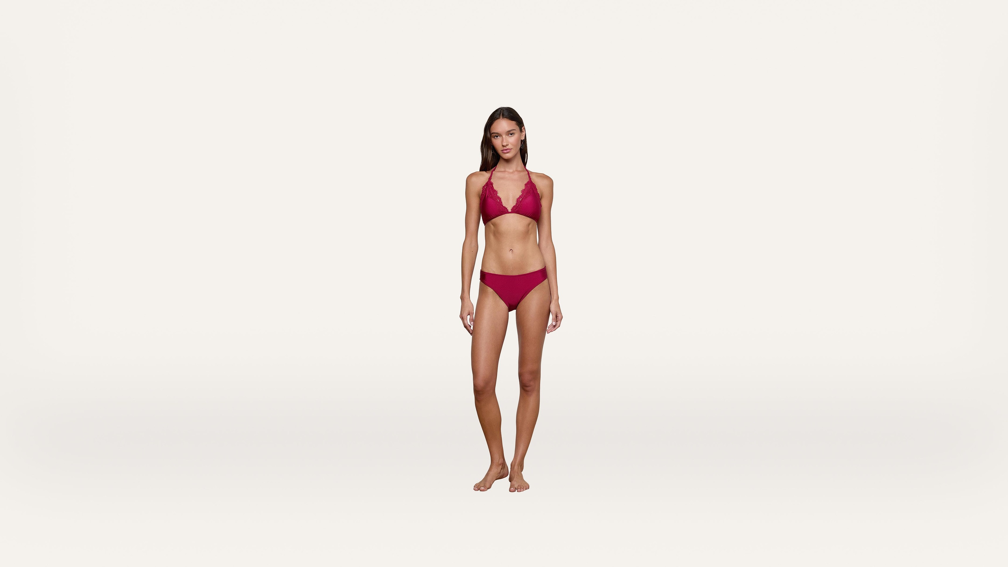 A woman stands barefoot on a plain white background, wearing a red bikini.