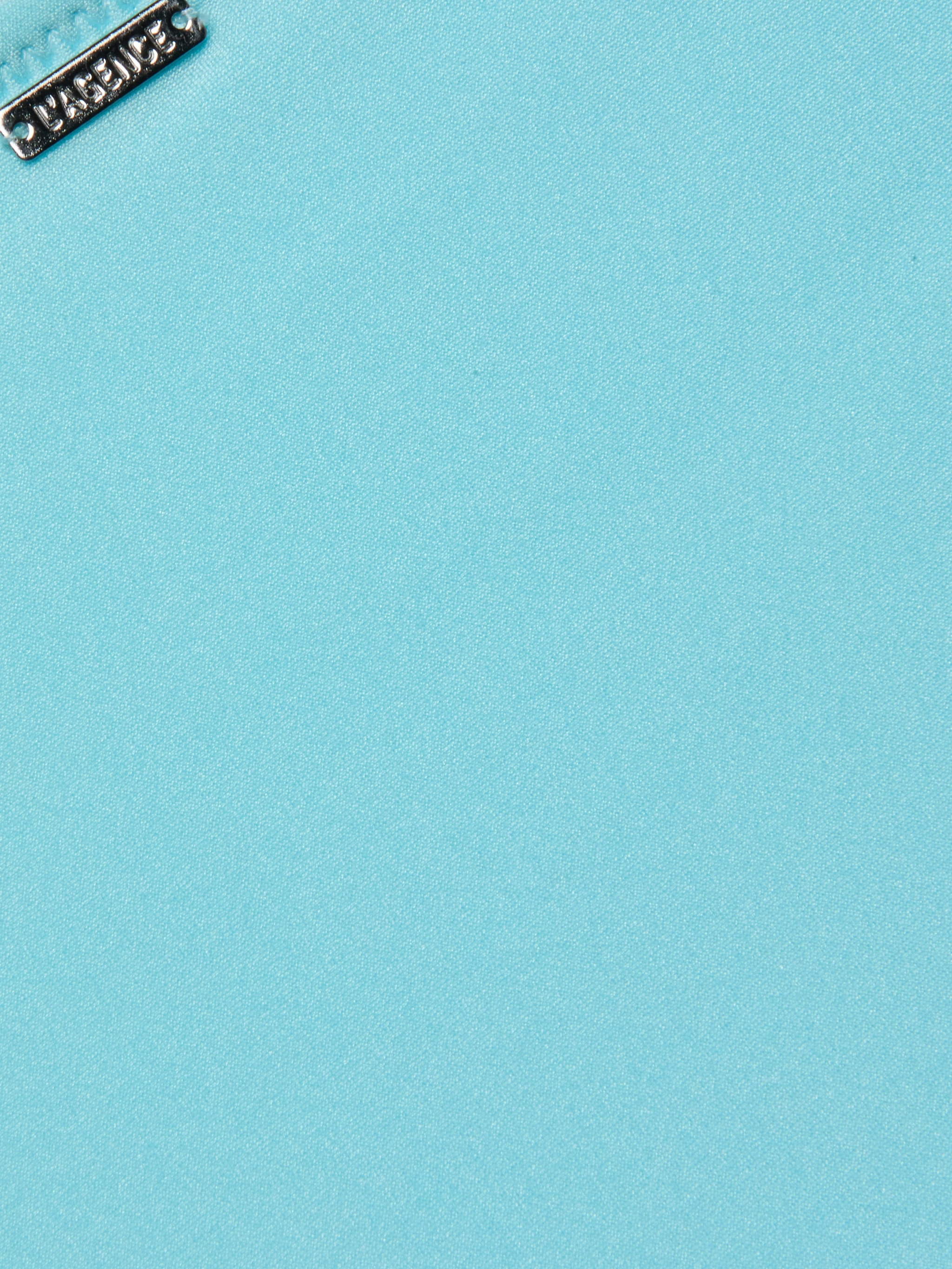 Close-up of a silver metallic tag with embossed design on the Nicole Bikini Bottom in ice blue. The tag is positioned near the top left corner, highlighting the smooth texture of the stretch nylon fabric.
