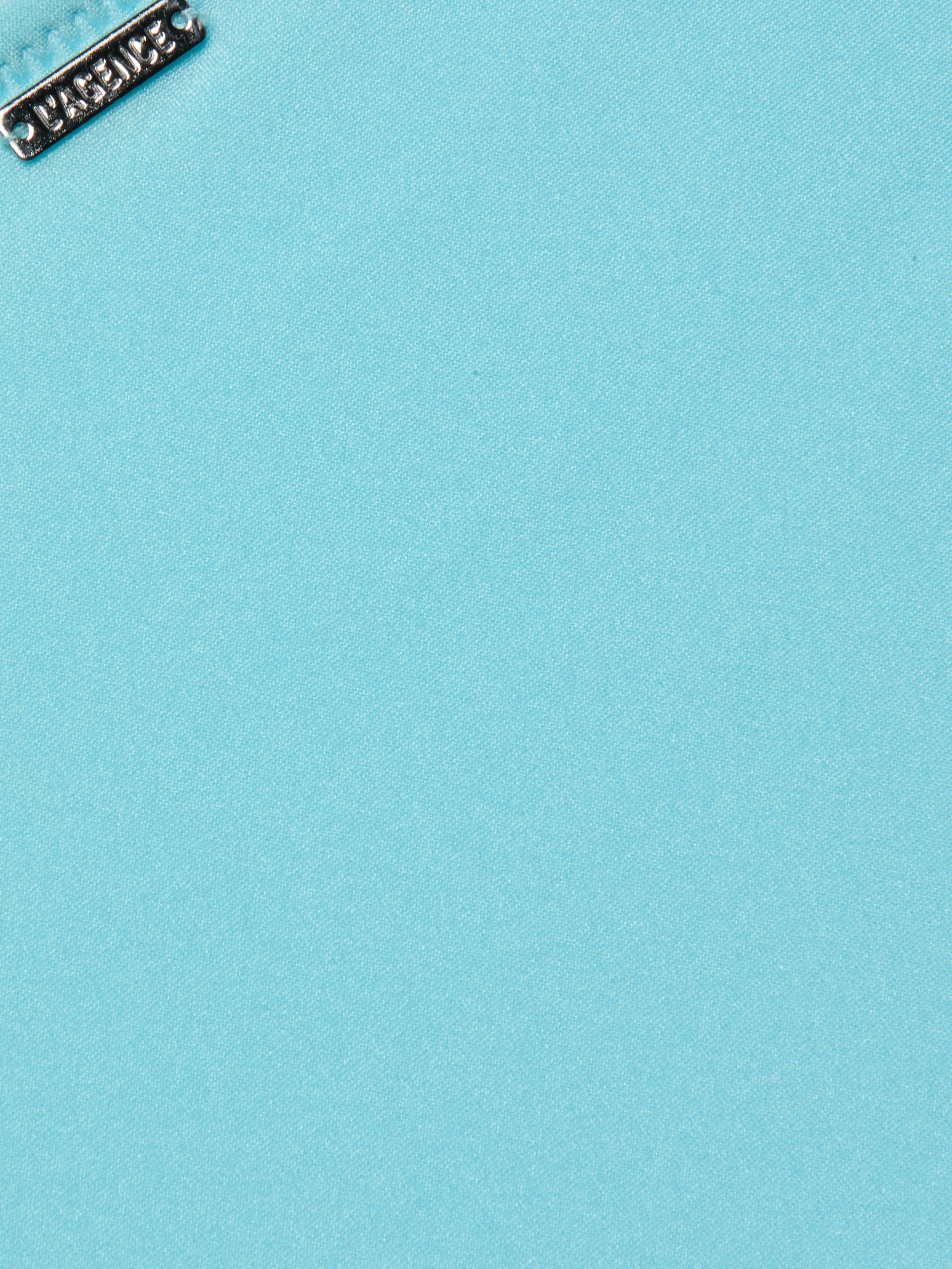 Close-up of a silver metallic tag with embossed design on the Nicole Bikini Bottom in ice blue. The tag is positioned near the top left corner, highlighting the smooth texture of the stretch nylon fabric.