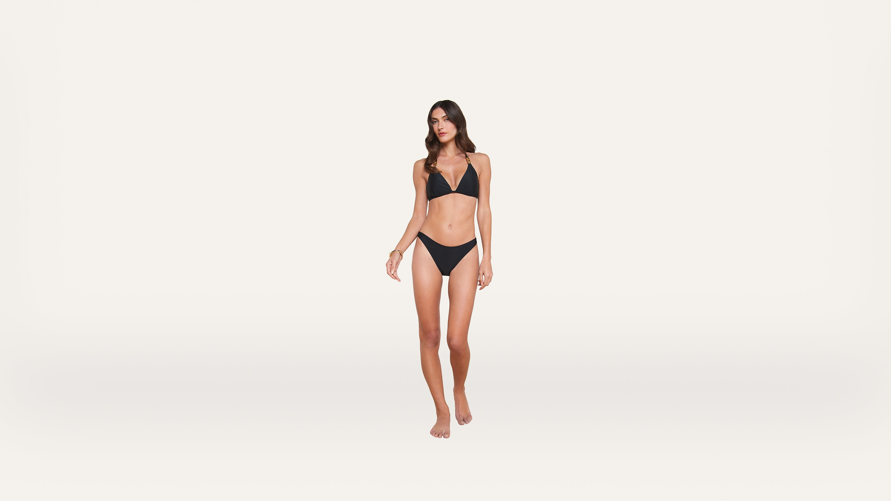 Woman in a black bikini stands barefoot against a plain white background, facing forward with a relaxed expression and posture.