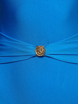 A close-up of the Lisa Plunge One-Piece Swimsuit in bright blue, showcasing moderate coverage and a gathered center accentuated by a round, gold decorative button with an intricate design.