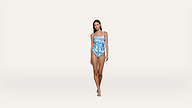 A woman stands facing forward wearing a blue and white patterned one-piece swimsuit against a plain, light background.