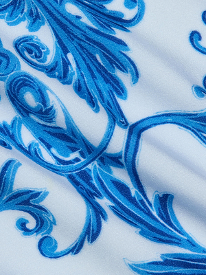 Close-up of the Remi One-Piece Swimsuit’s white fabric, featuring an intricate blue floral and leaf design that evokes a baroque print. The smooth texture and subtle folds highlight its luxe, elegant feel.